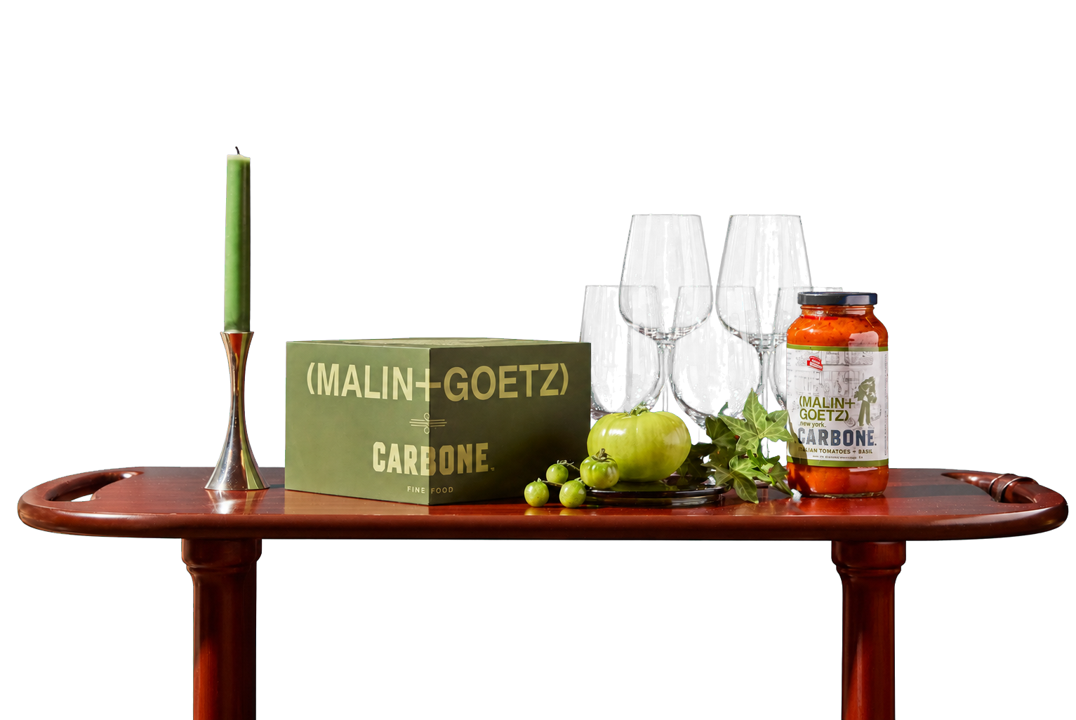 A wooden drink cart with the MALIN+GOETZ X Carbone box, glasses and sauce jar in front of a red curtain