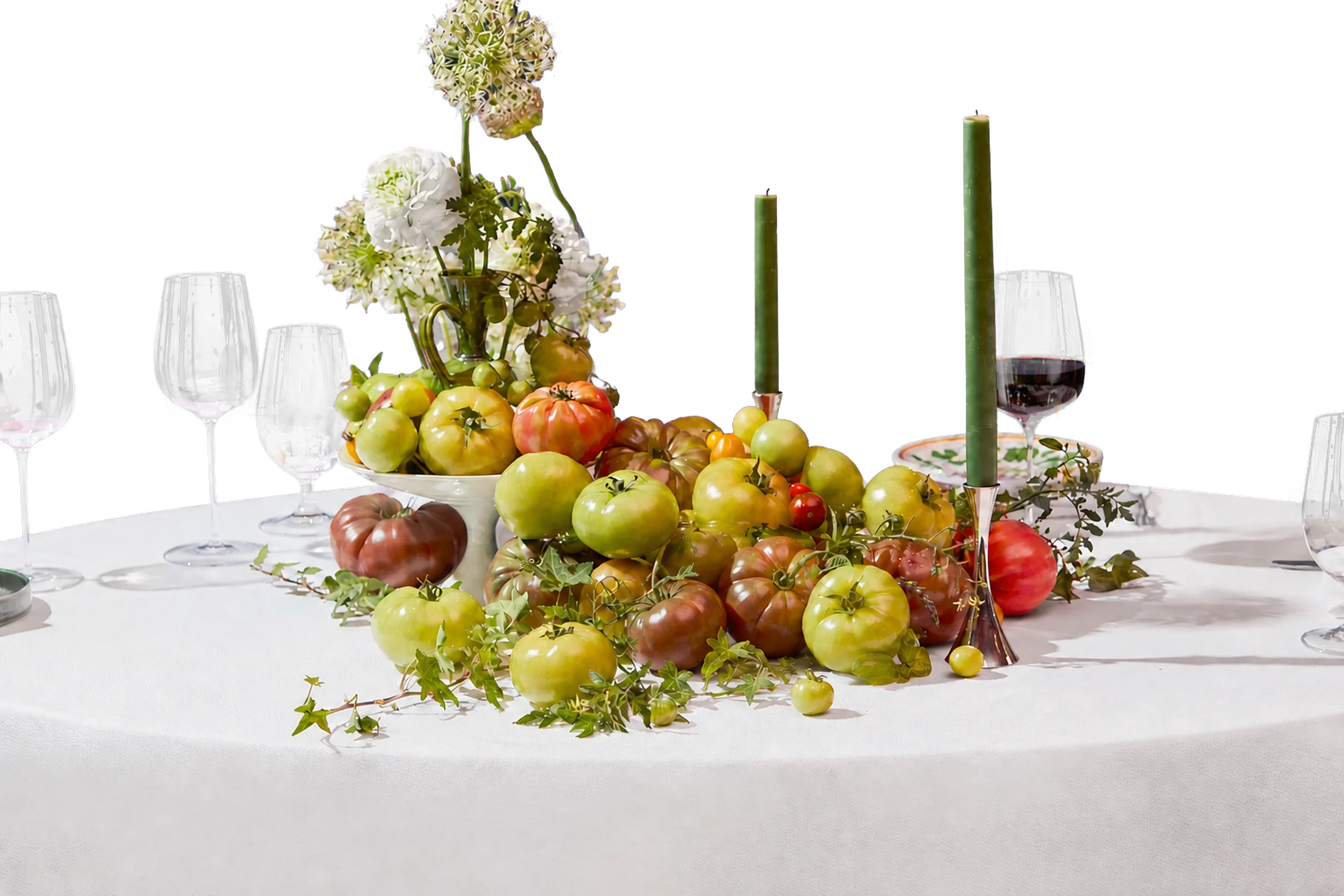 A set dinner table with heirloom tomatoes, flowers and green taper candles